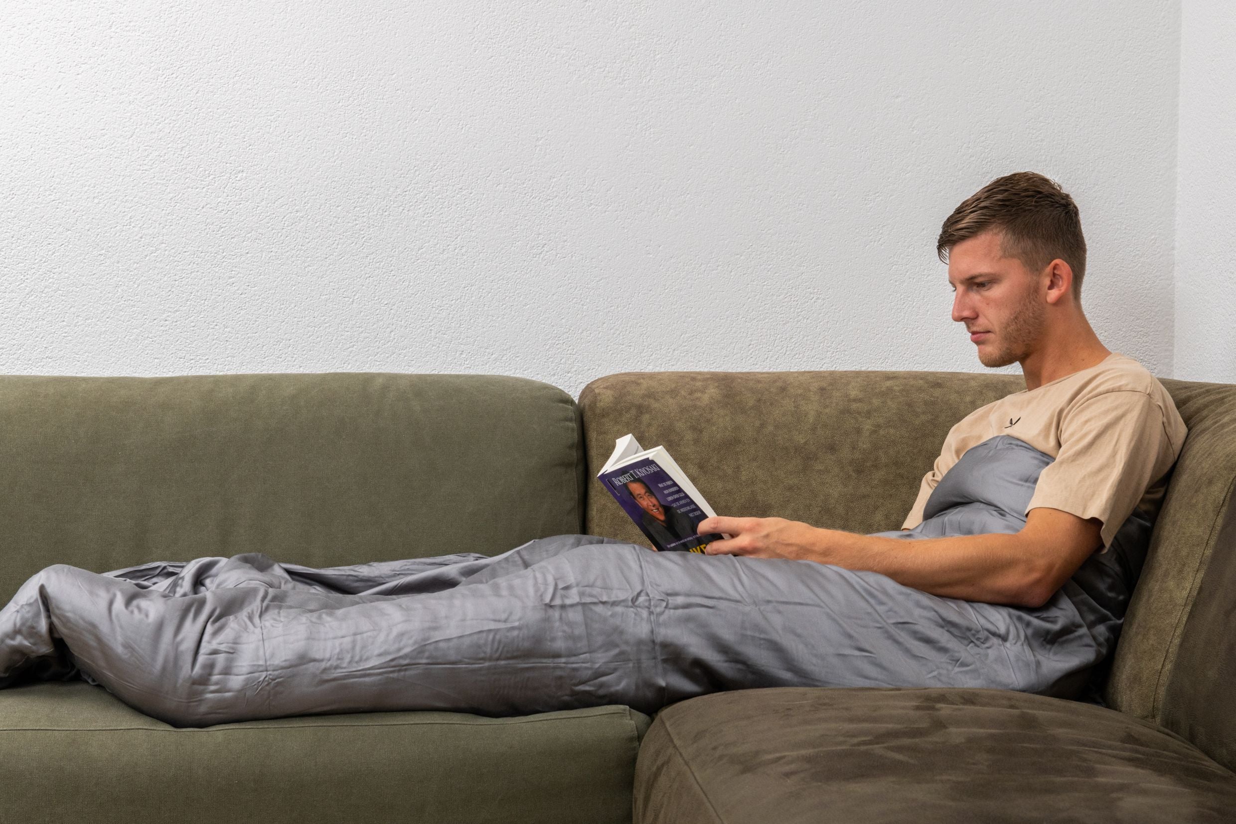 man met verzwaringsdeken op bank met boek